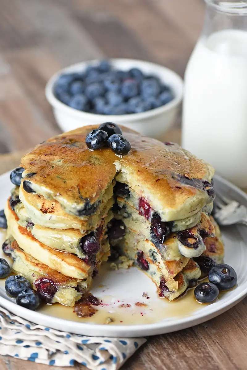 Sliced Blueberry Buttermilk Pancakes with maple syrup on a plate, paired with fresh blueberries and milk on the side