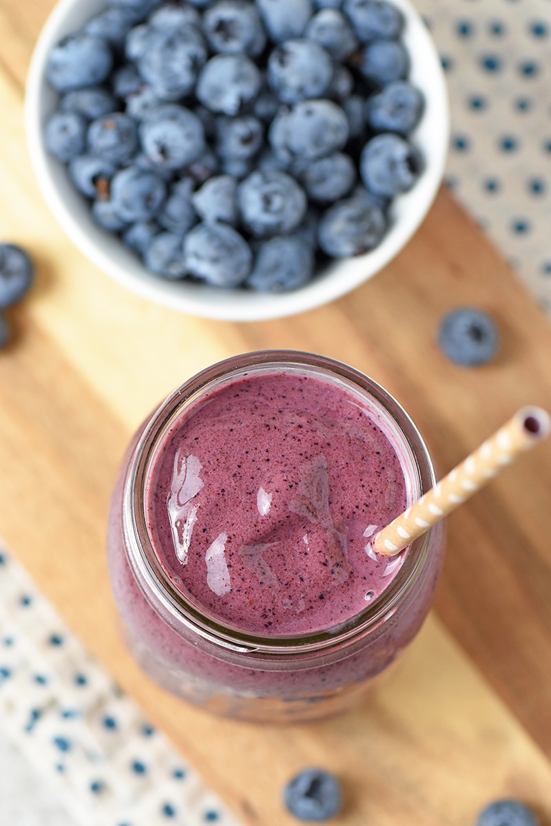 Blueberry Spinach Smoothie in mason jar with straw on wooden cutting board with fresh blueberries and blue polka dot cloth