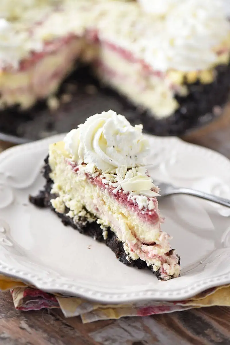 slice of raspberry swirl cheesecake with white chocolate and whipped cream on white plate