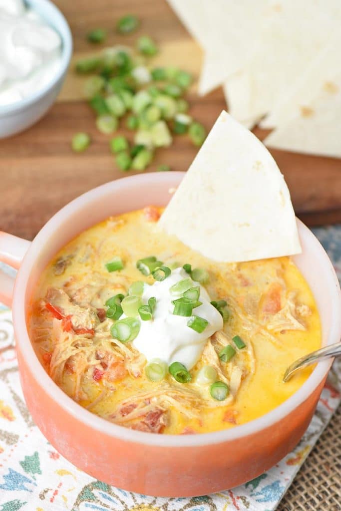 orange Fire-King soup bowl with chicken enchilada soup, tortilla triangle, sour cream, and green onions