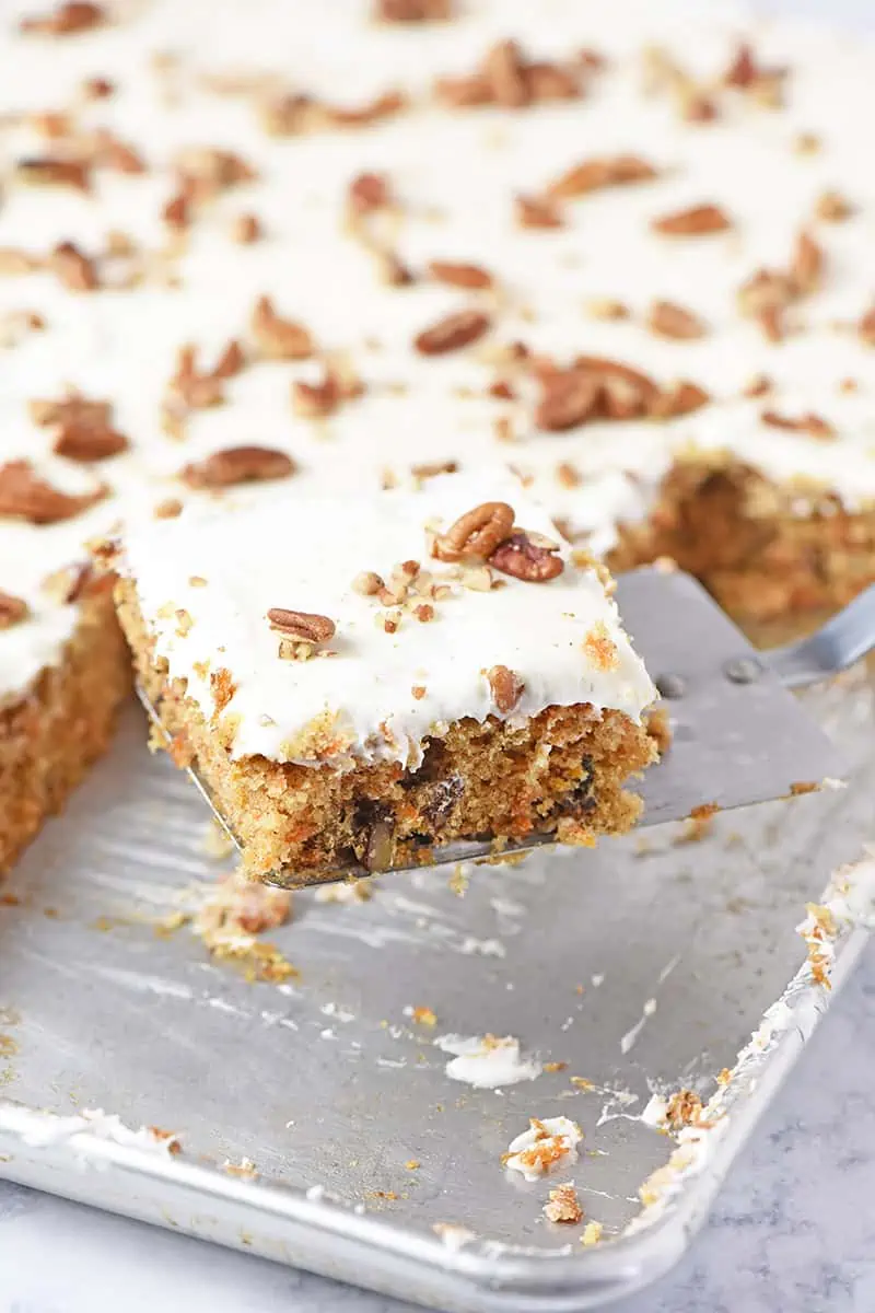 Slice of carrot sheet cake with cream cheese frosting and pecans on a spatula