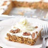 cream cheese frosting swirl on slice of carrot cake on white plate with fork