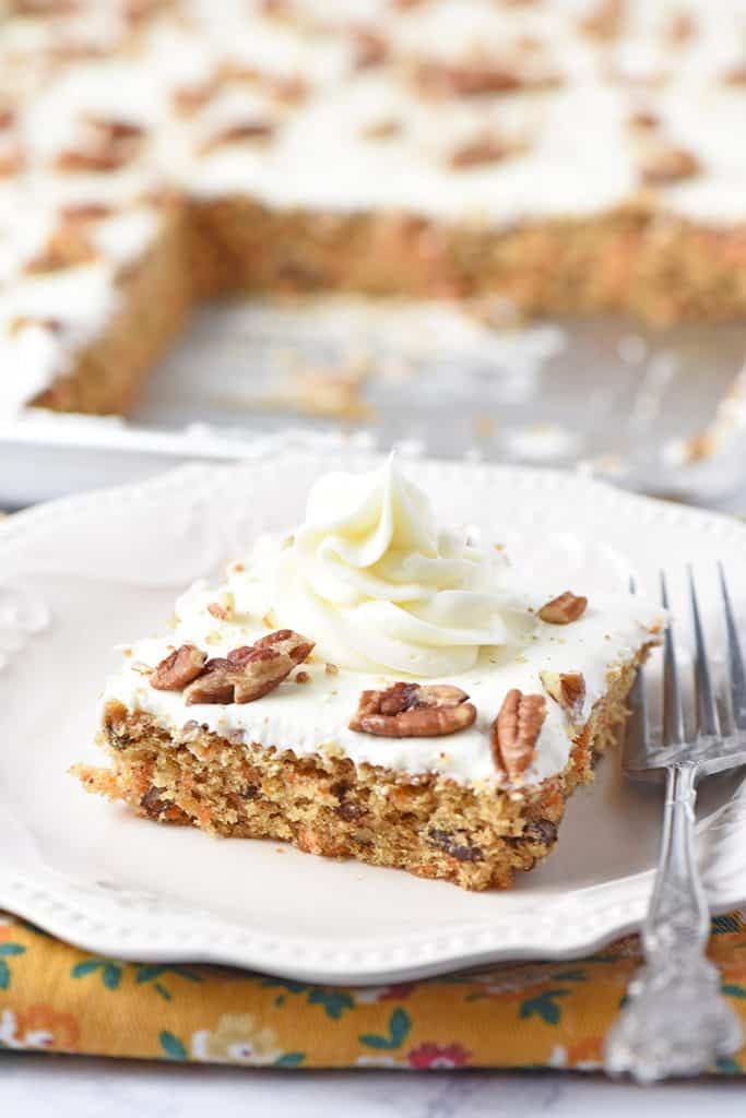 cream cheese frosting swirl on slice of carrot cake on white plate with fork