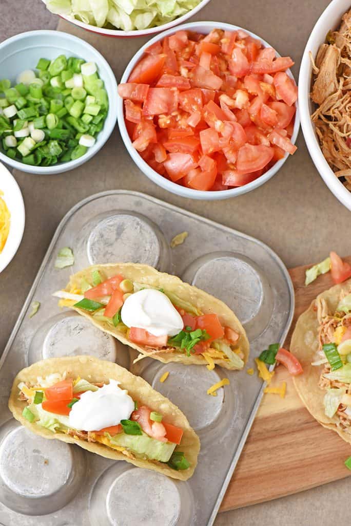 shredded chicken tacos with fresh ingredients on a muffin pan