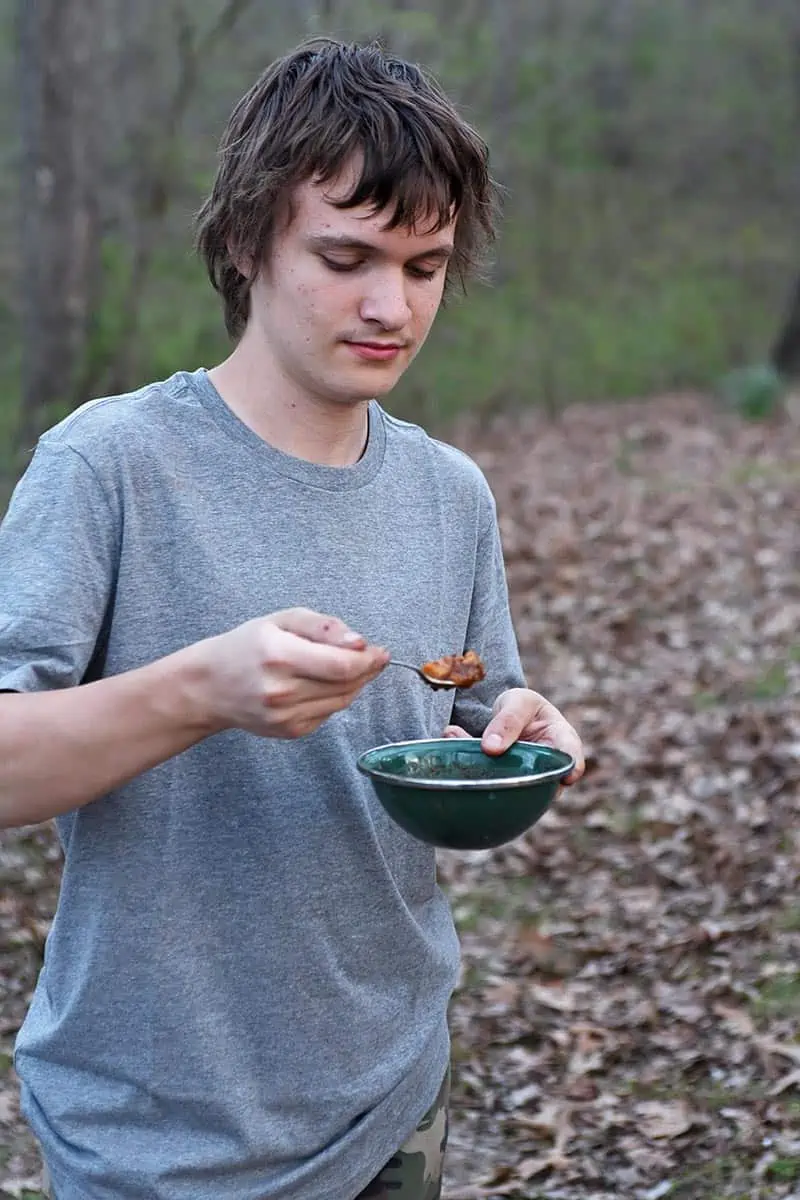 boy taking bite of beef stew with camping cooking gear like real bowls and eating utensils