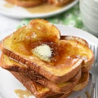 French toast on a plate with butter and maple syrup and a mug of milk