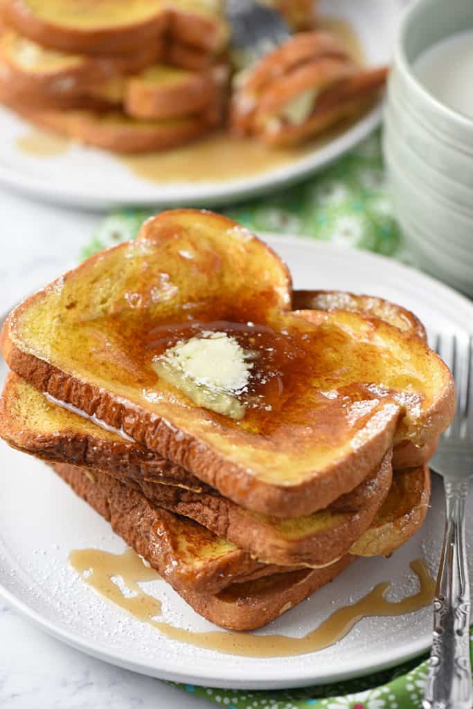 French toast on a plate with butter and maple syrup and a mug of milk