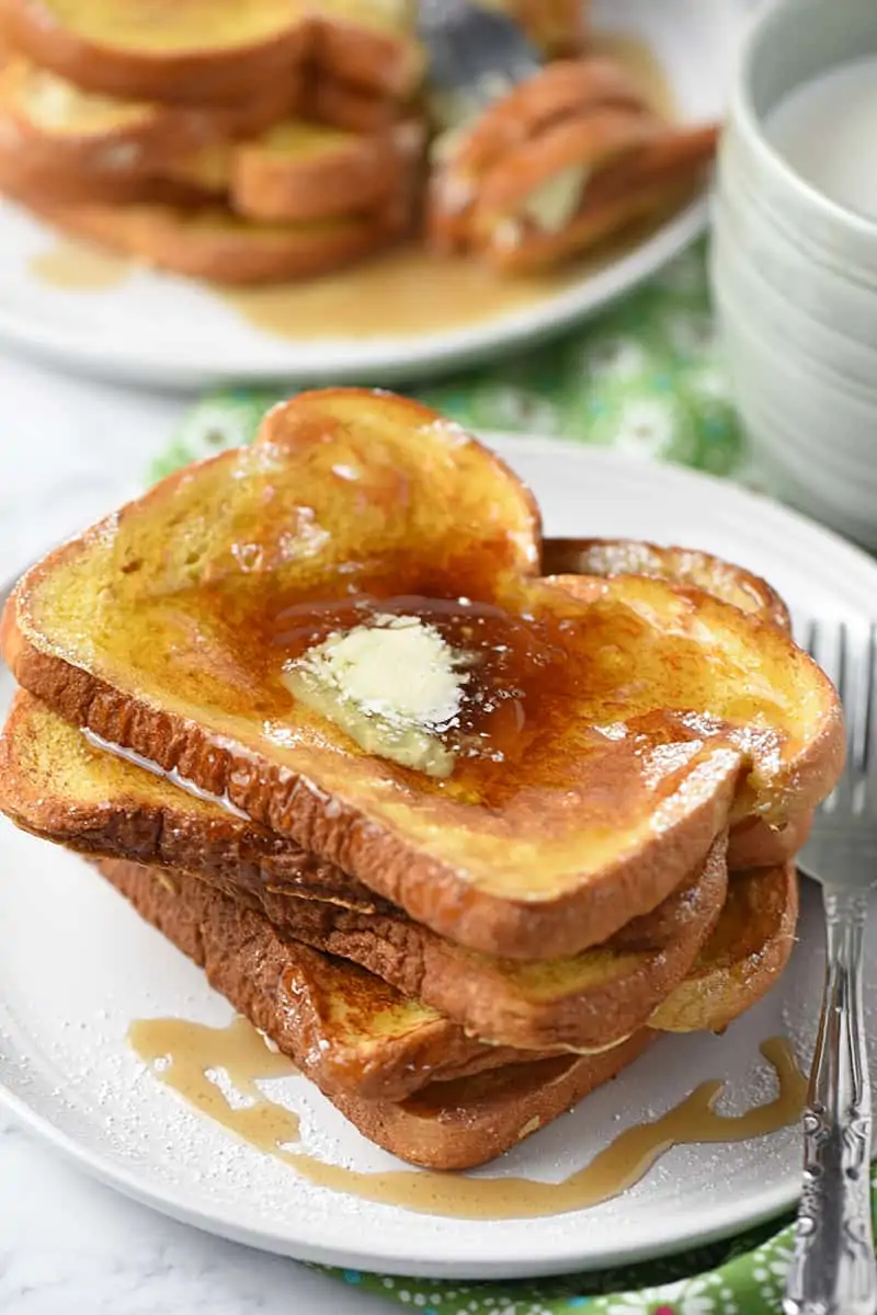 French toast on a plate with butter and maple syrup and a mug of milk