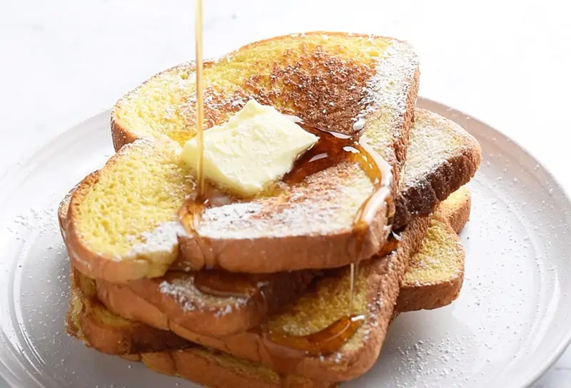 Pile of the best French toast recipe with butter and maple syrup, pouring syrup on