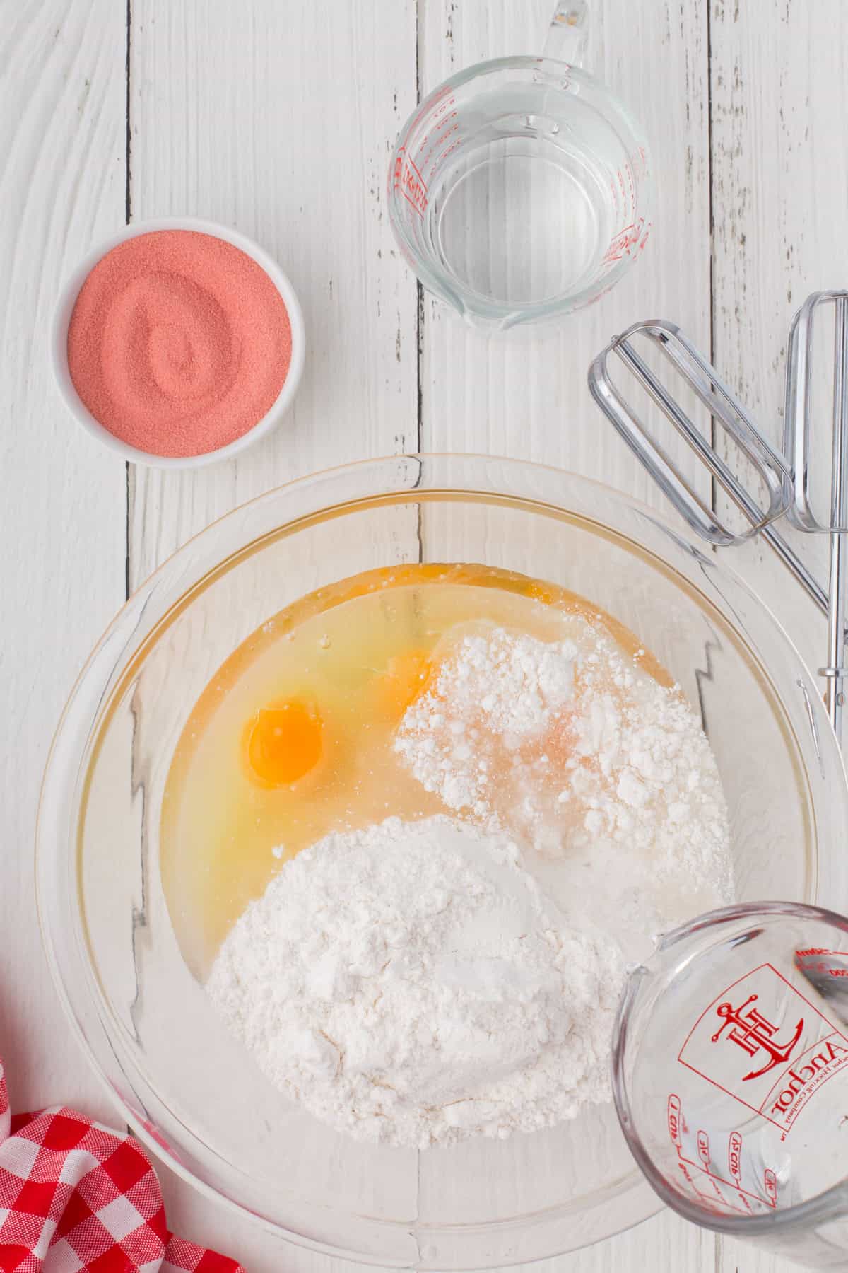 mixing up a moist white cake mix with eggs and canola oil in a large glass mixing bowl to make strawberry Jello poke cake with an American flag design