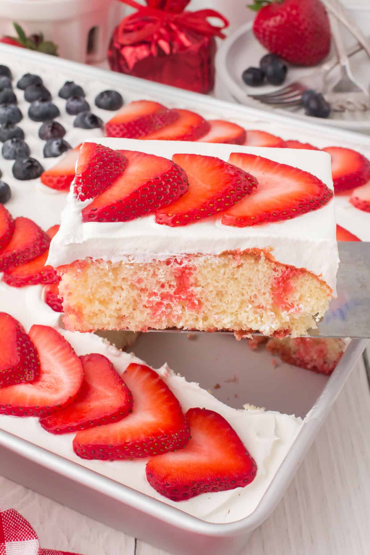 closeup photo showing a spatula holding up a slice of flag cake with fresh sliced strawberries on top