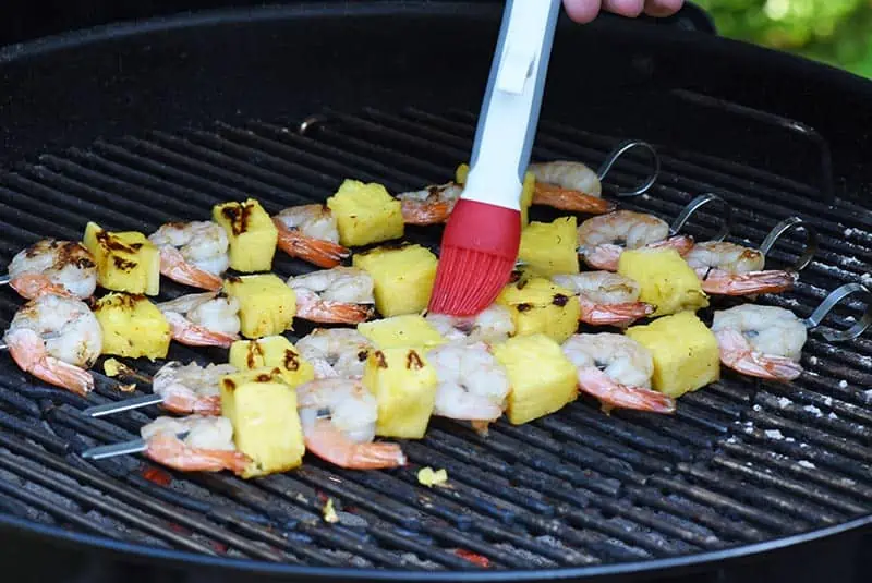 brushing a maple bourbon grilled shrimp marinade or glaze on shrimp kabobs on the charcoal grill