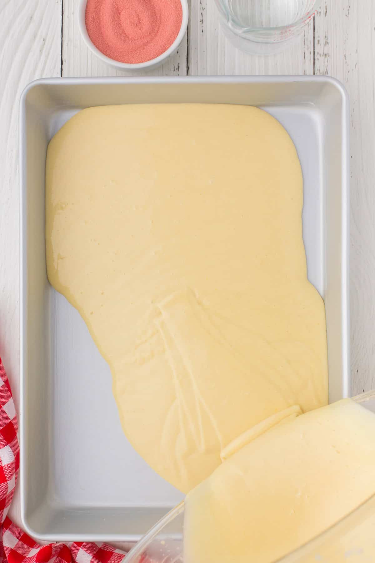 pouring a white cake mix into a 9x13 baking dish to make strawberry Jello poke cake