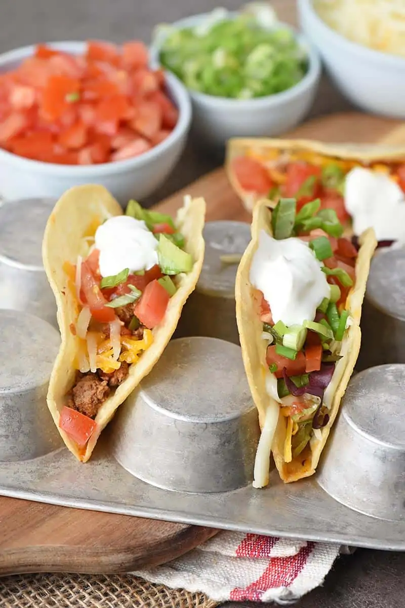 beef tacos in corn tortilla taco shells set in a muffin pan for filling with all the toppings