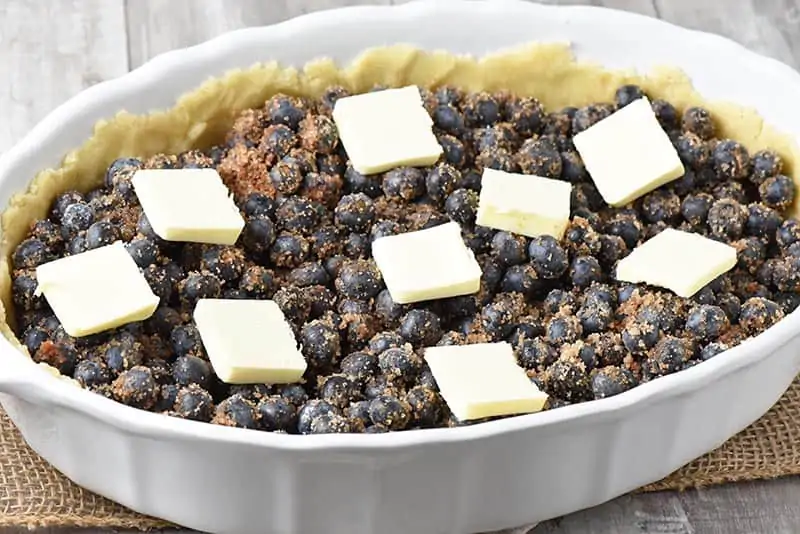 butter slices on top of blueberry cobbler in white baking dish
