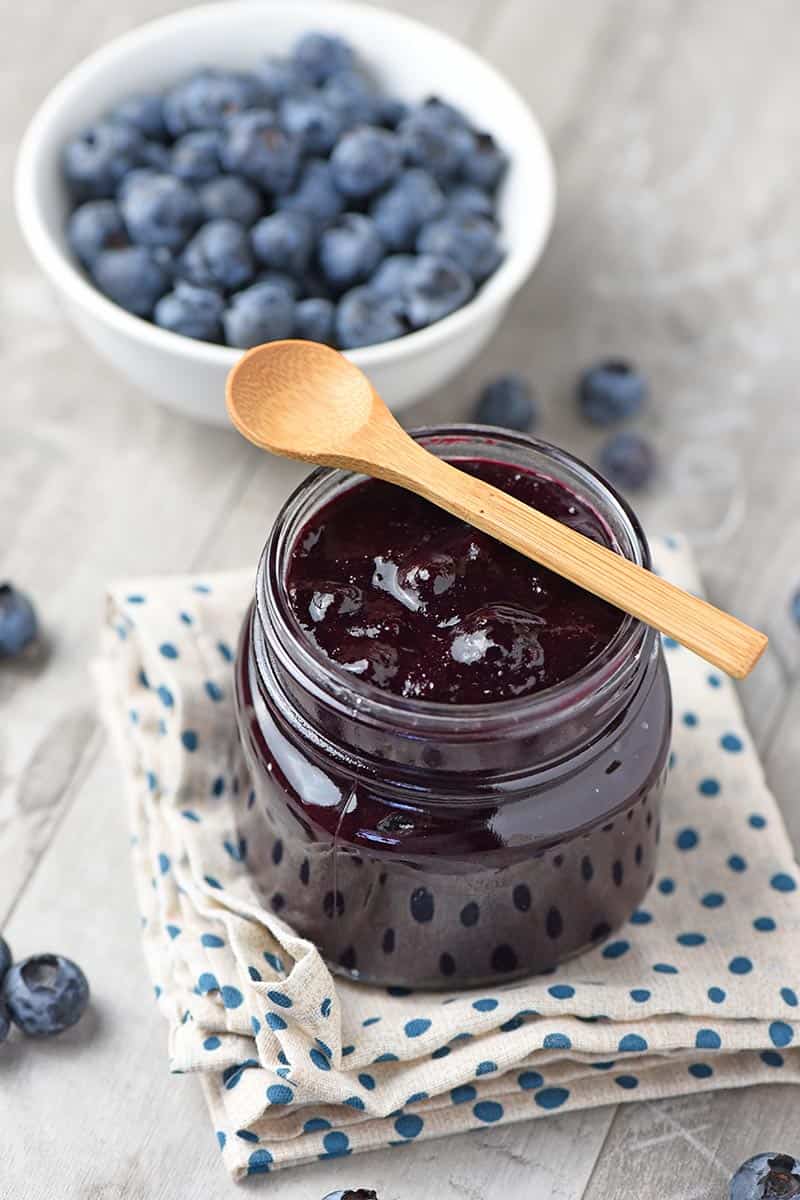 blueberry filling for pie in a mason jar with a wooden spoon and fresh blueberries