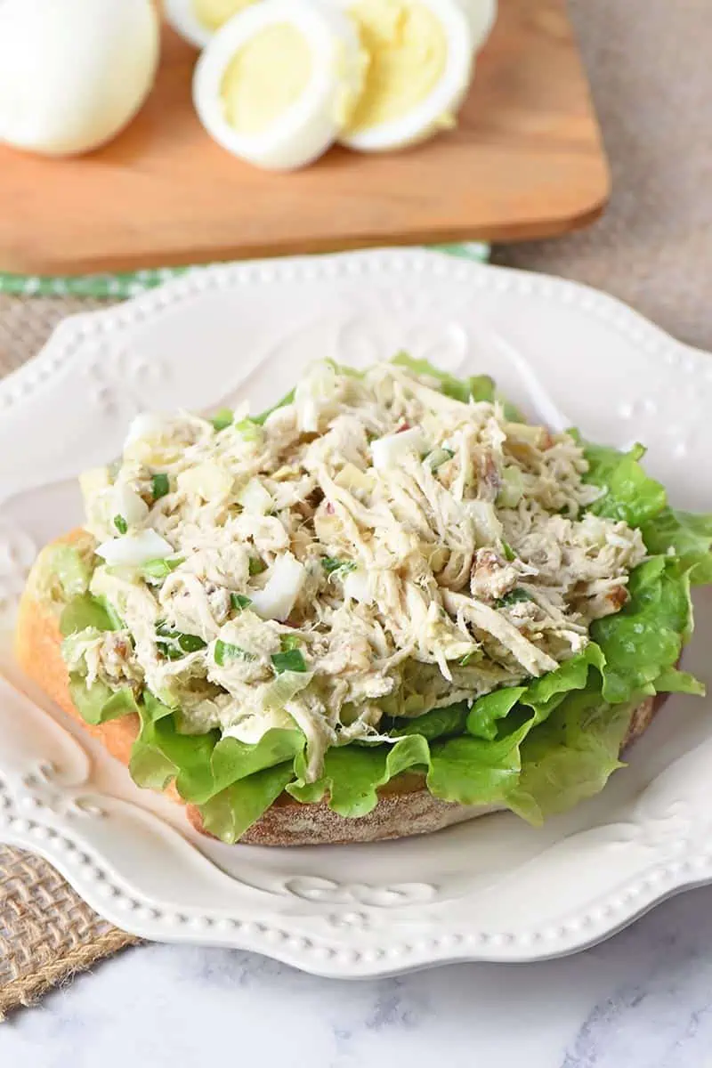 chicken salad with apples open-faced sandwich on white plate with hard boiled eggs on a small wooden cutting board