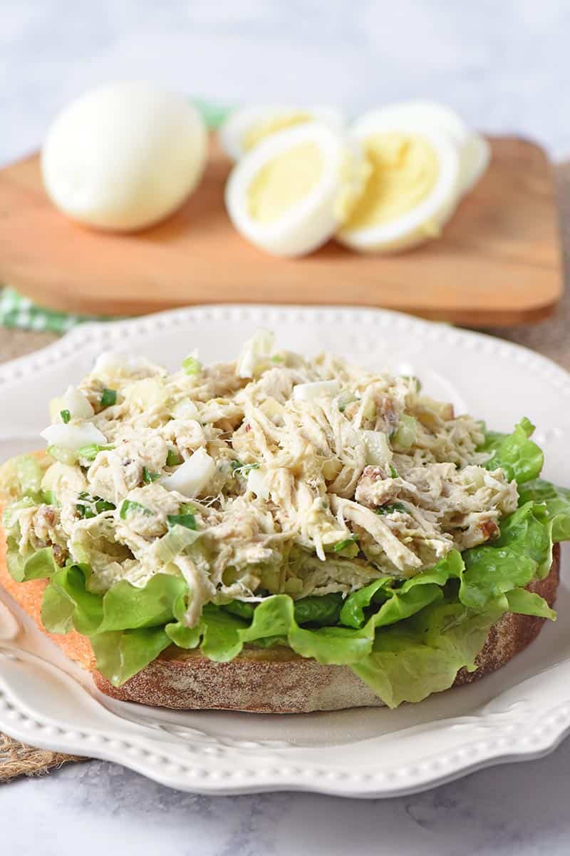 chicken salad recipe with eggs and apples on slice of sourdough with lettuce, on white plate