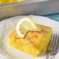 slice of lemon poke cake with lemon glaze on white plate with slice of lemon on top
