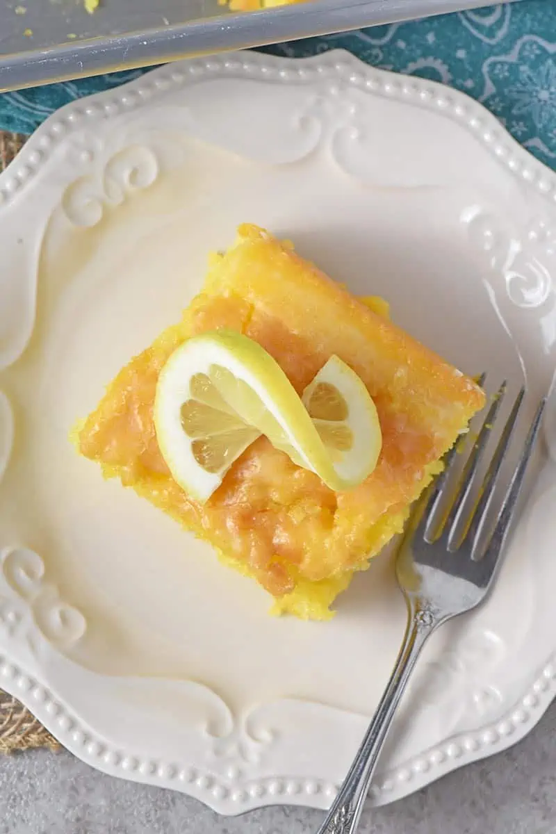 slice of lemon cake on white plate with slice of lemon and a fork