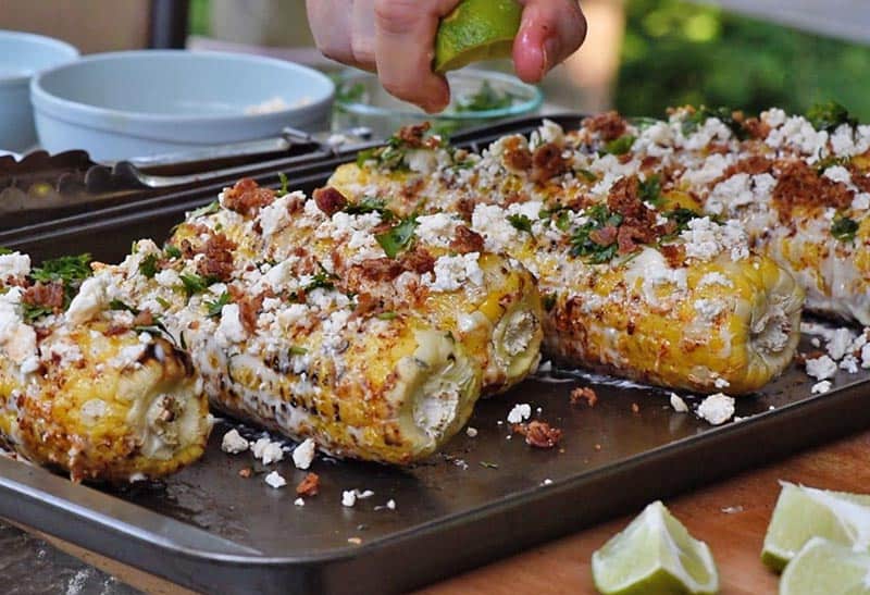 squeezing lime juice onto ears of grilled Mexican corn on the cob