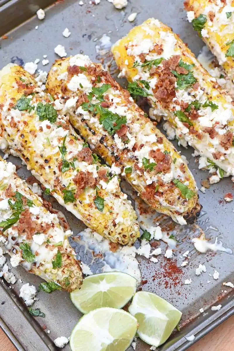 grilled Mexican corn on the cob on baking sheet with lime wedges