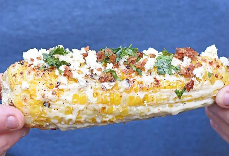 Grilled ear of Mexican corn on the cob with all the fixings, including mayo, Feta cheese, cilantro, and bacon