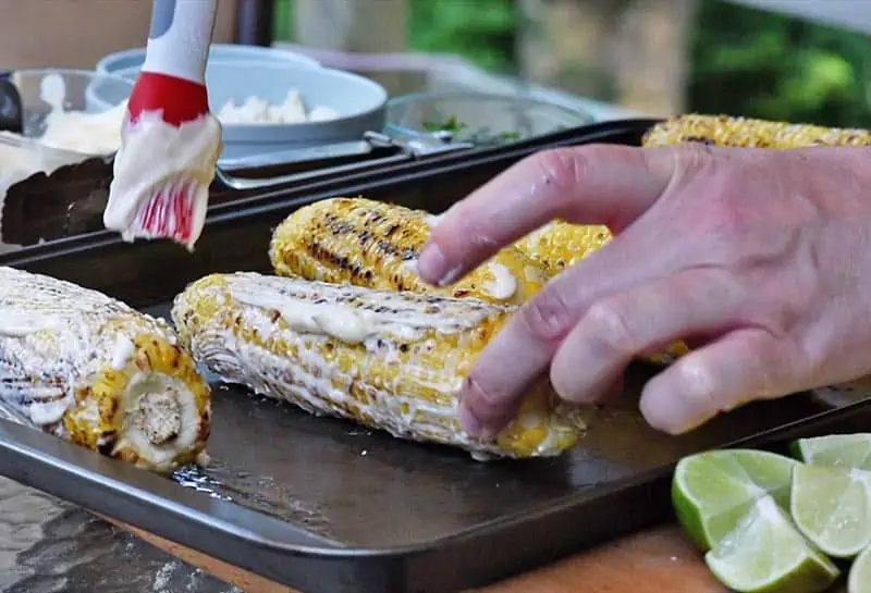brushing mayo onto ears of grilled corn with basting brush for mexican street corn recipe