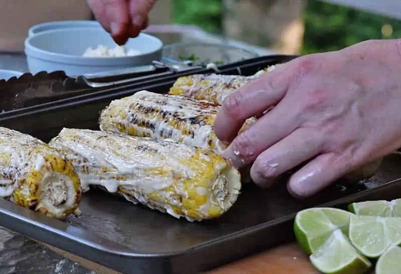 sprinkling chili powder on grilled corn for Mexican corn recipe