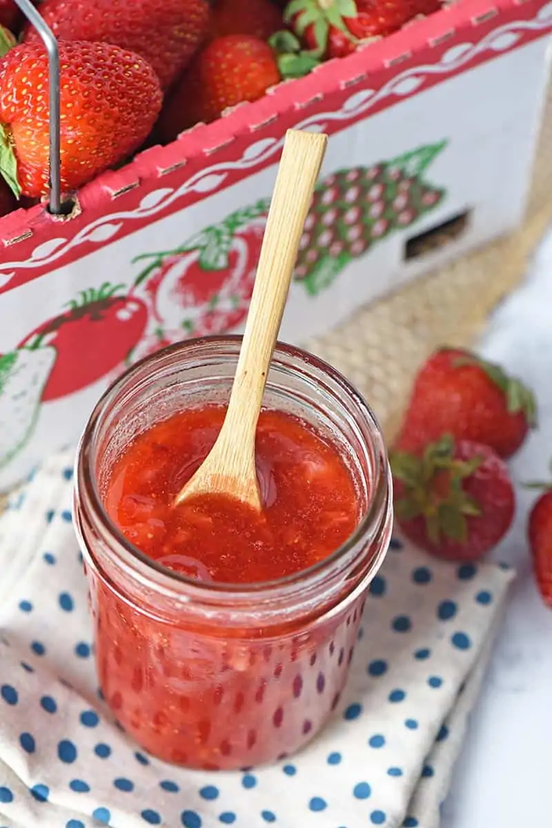no cook strawberry jam recipe that's quick and easy to make, jam in a jar with a small wooden spoon