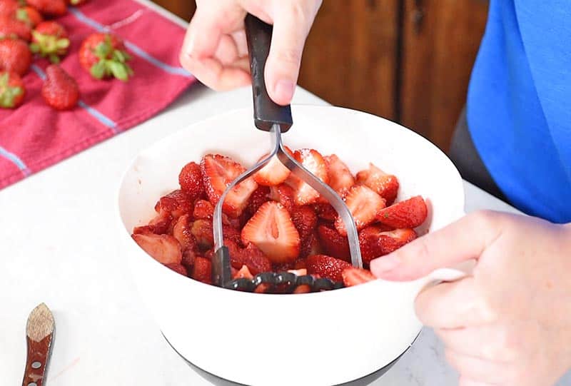crushing strawberries with a potato masher for a quick and easy strawberry jam recipe