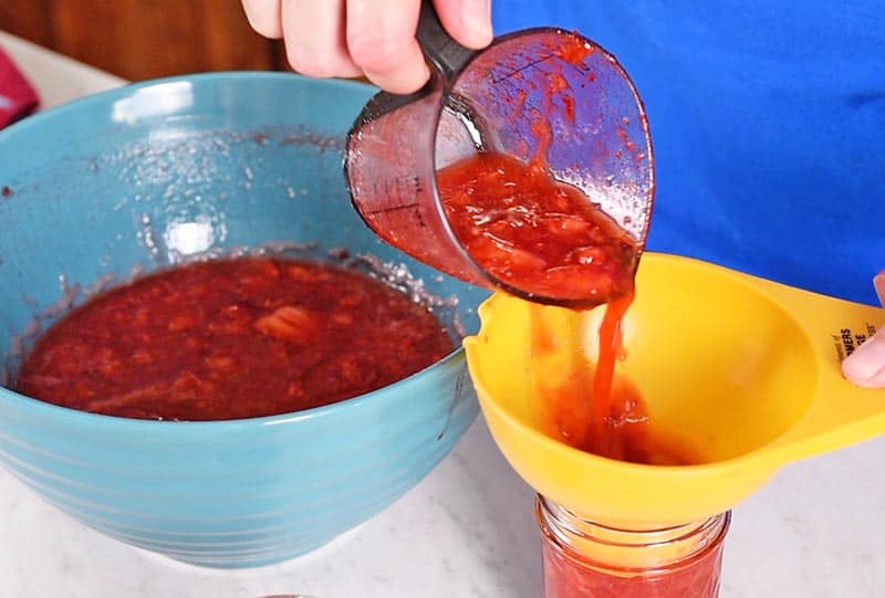 pouring strawberry freezer jam in jelly jars using a jar funnel