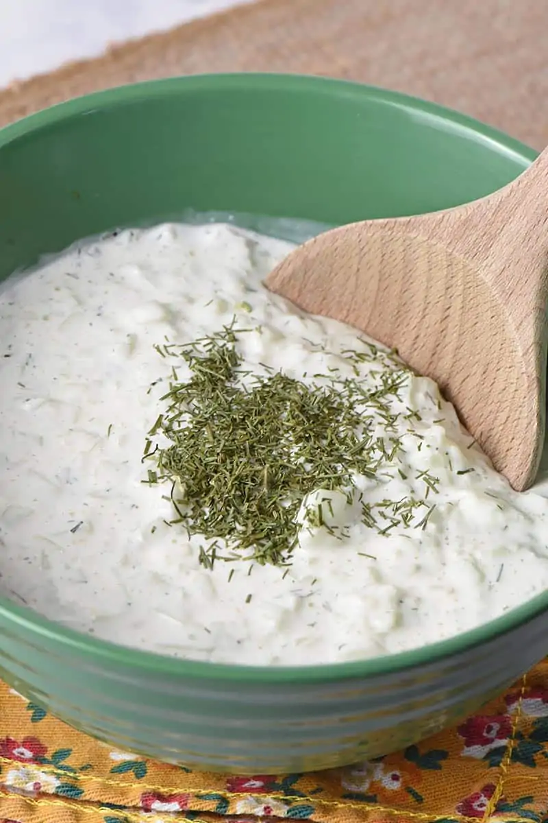 easy recipe for tzatziki sauce in green bowl with wooden spoon