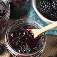 close up jar of homemade blackberry jam with tiny wooden spoon and fresh blackberries