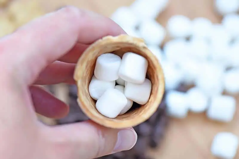 mini marshmallows layered with chocolate chips in an ice cream cone for s'mores cones recipe