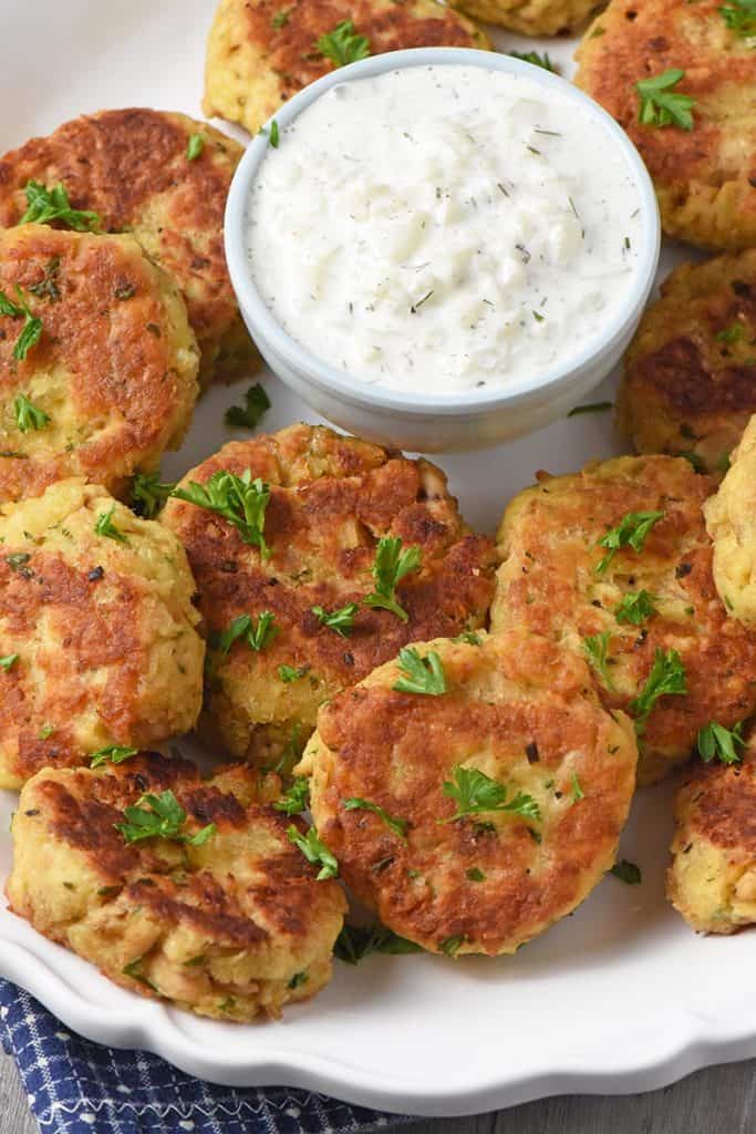 delicious salmon patties on white platter with small bowl of tzatziki sauce