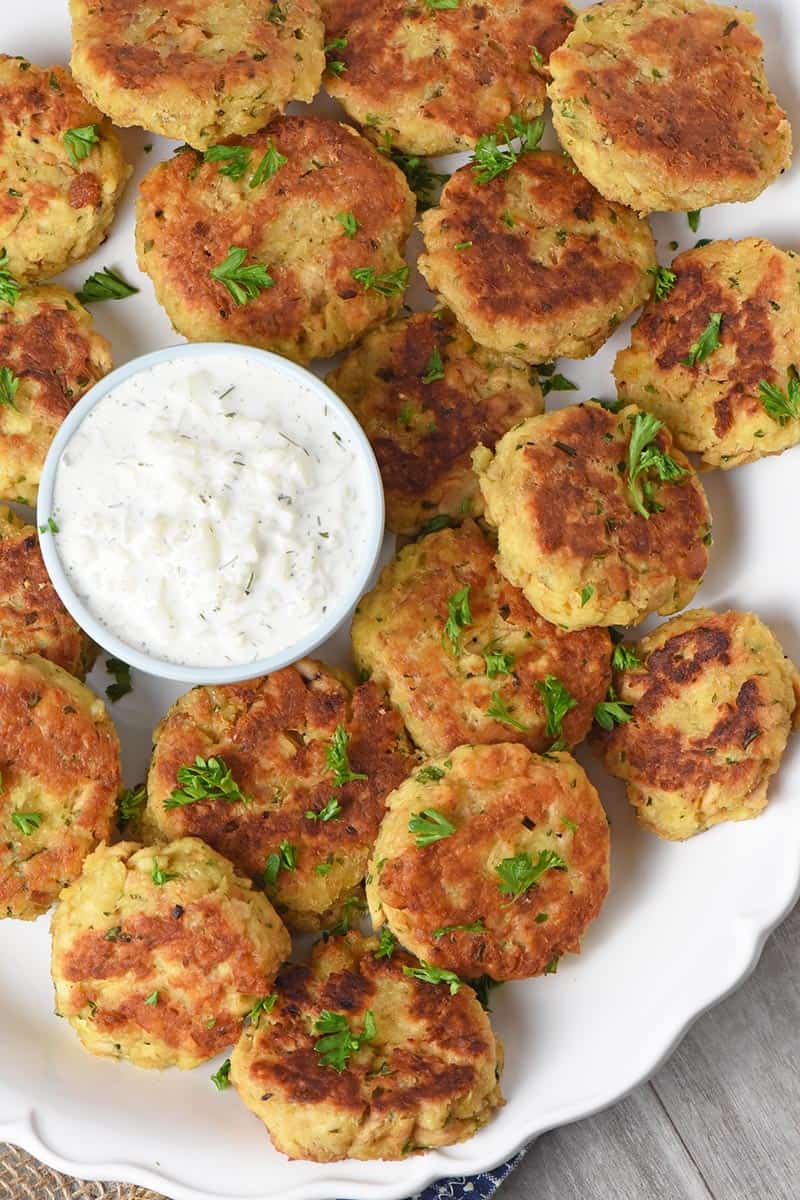fried salmon patties on a white serving platter with small bowl of tzatziki sauce