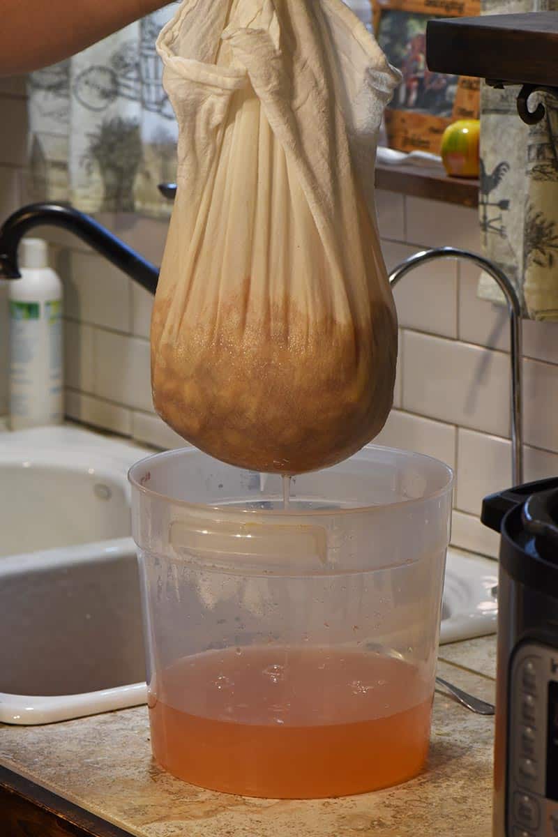 straining homemade apple juice with a flour sack towel and bucket