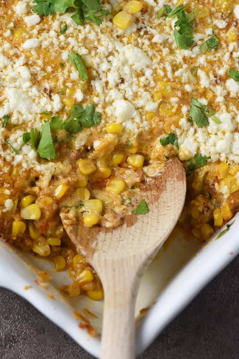 wooden spoon dishing up Mexican corn casserole from white casserole dish