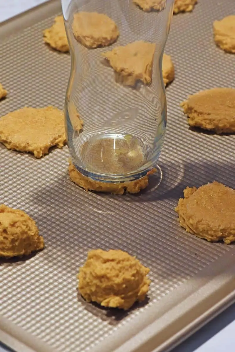 flattening soft pumpkin sugar cookies with the bottom of a glass coated in cane sugar on cookie sheet