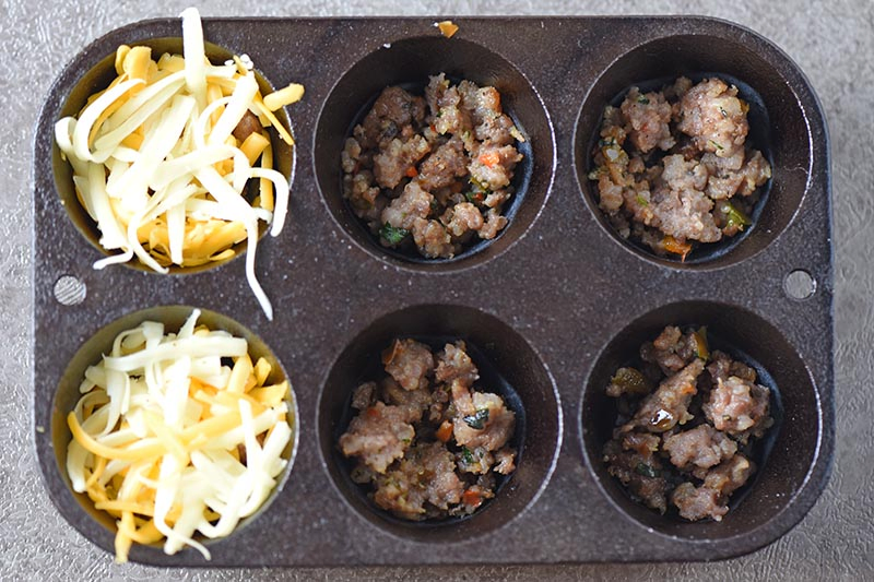 layering sausage and cheese for sausage egg muffins in cast iron muffin pan