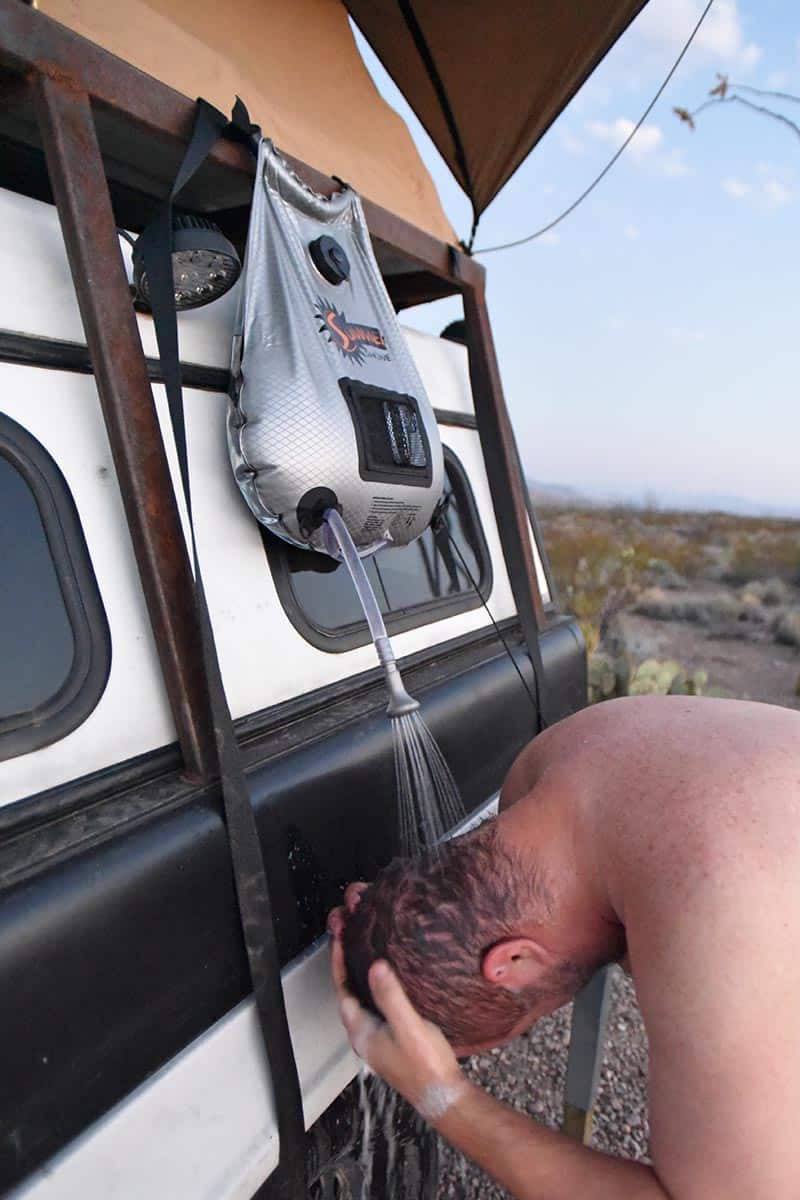 man washing hair with solar camping shower, perfect for backcountry camping and dispersed camping