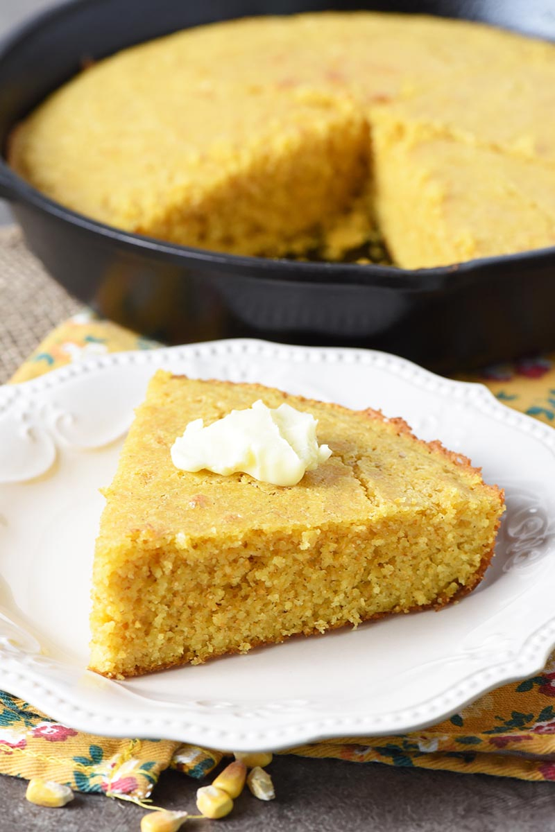 Slice of buttermilk cornbread with butter on white plate