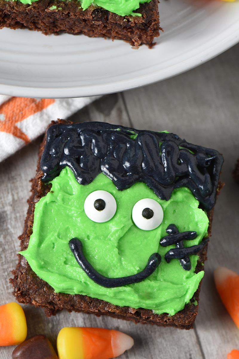Frankenstein brownies decorated with frosting and candy eyeballs on wood countertop with candy corn