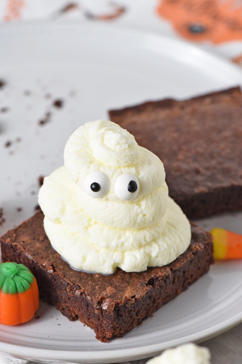 whipped cream and candy eyeballs ghost halloween brownies on a gray plate with candy corn and mellowcreme pumpkins