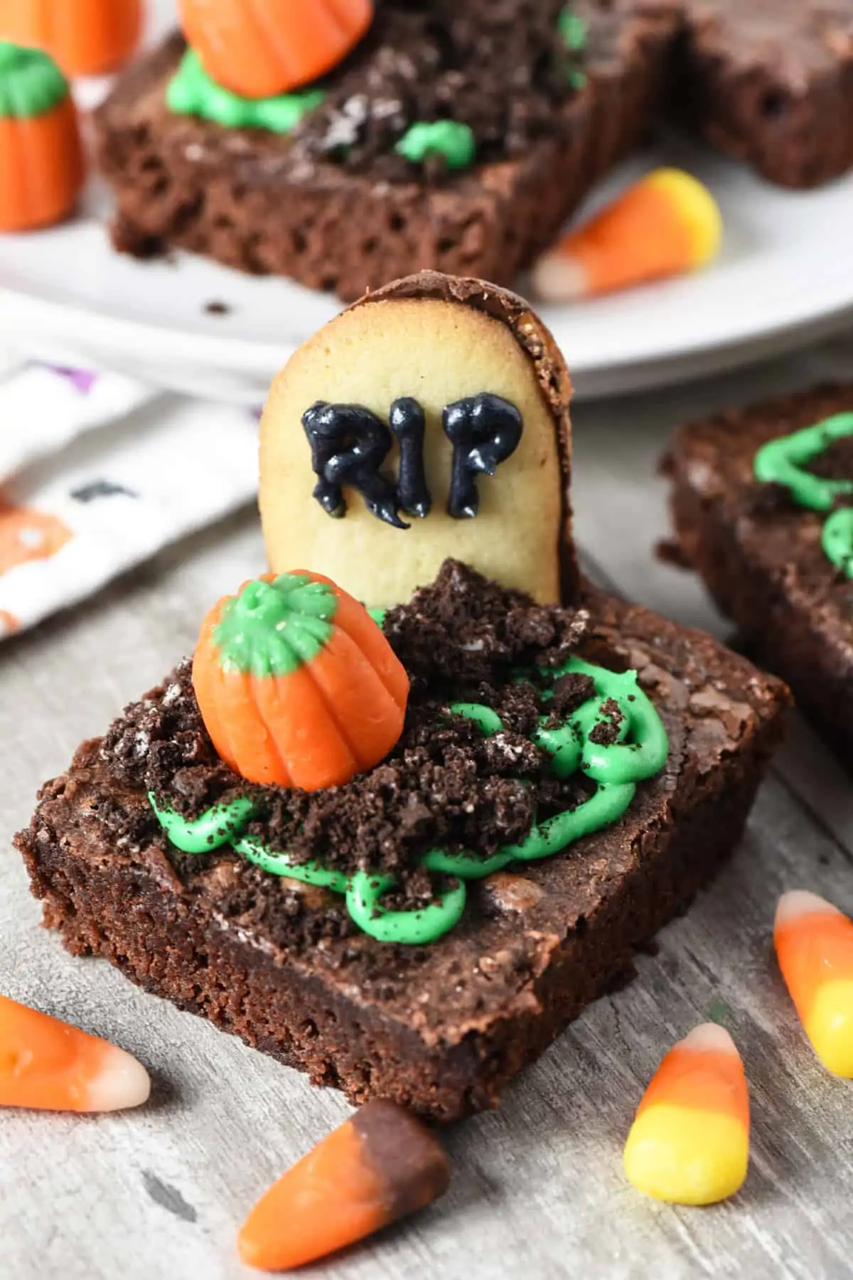 spooky graveyard brownies with Milano Cookies as gravestones, Oreos as dirt, green icing, and candy pumpkins