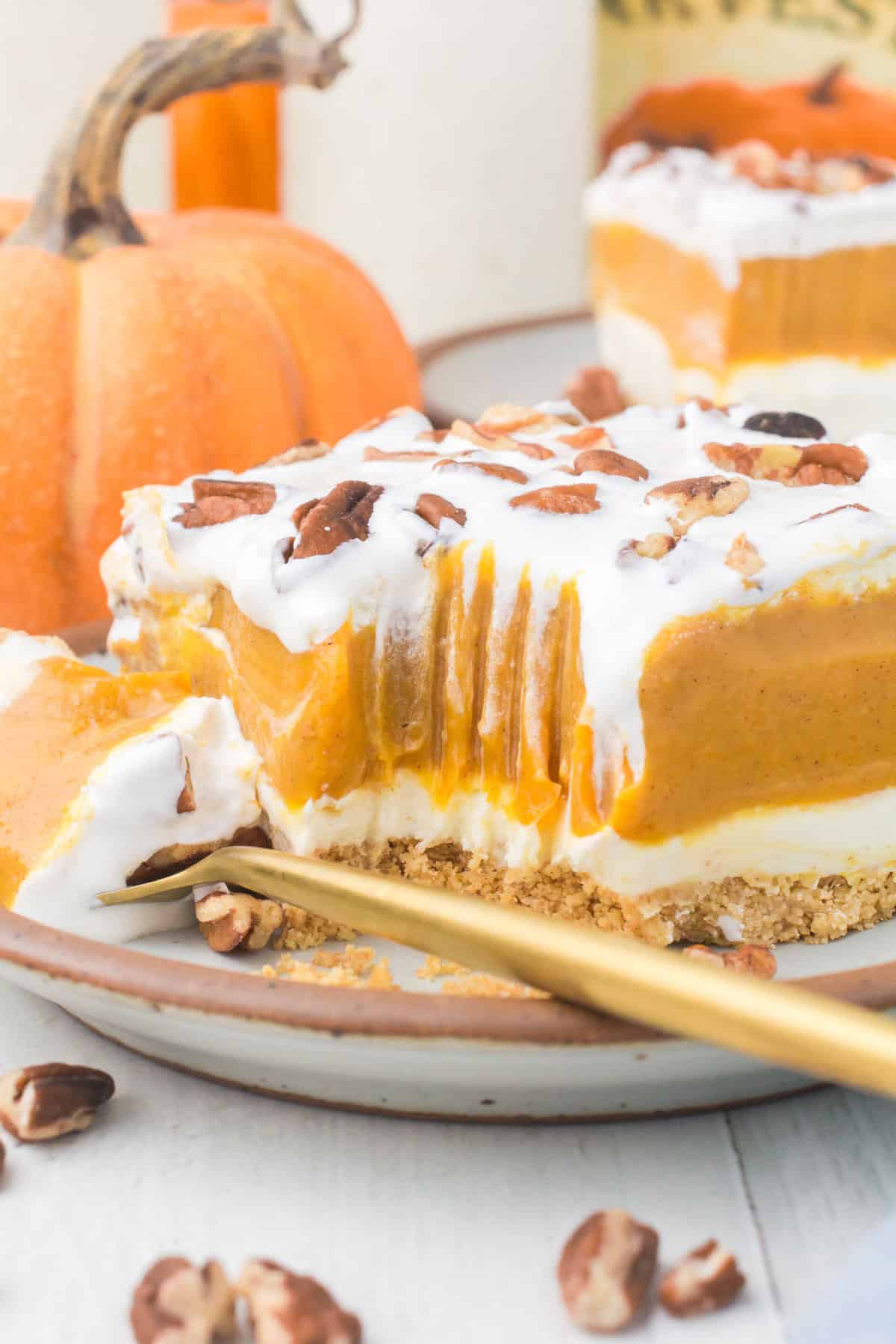 closeup photo showing a sliced square of no bake pumpkin delight on a small gray decorative plate with chopped pecans and Cool Whip on top