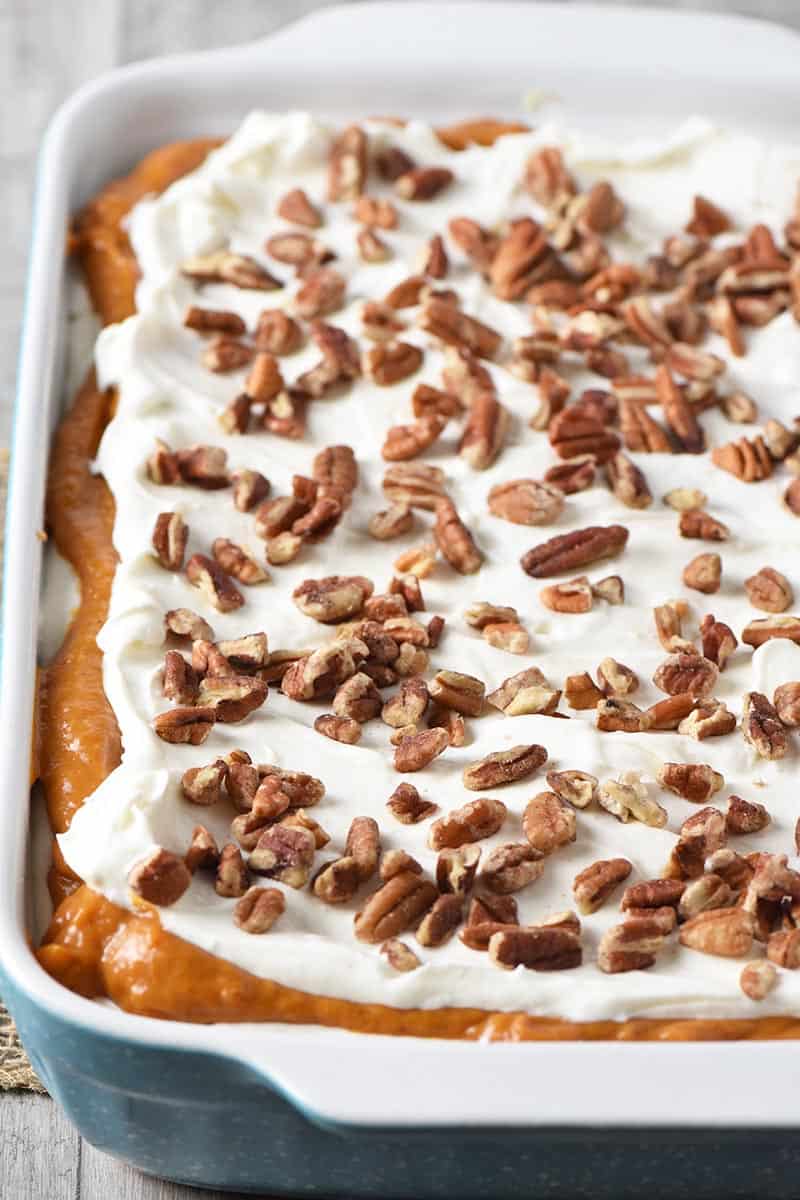 no bake pumpkin dessert with whipped cream and pecans on top in blue baking dish