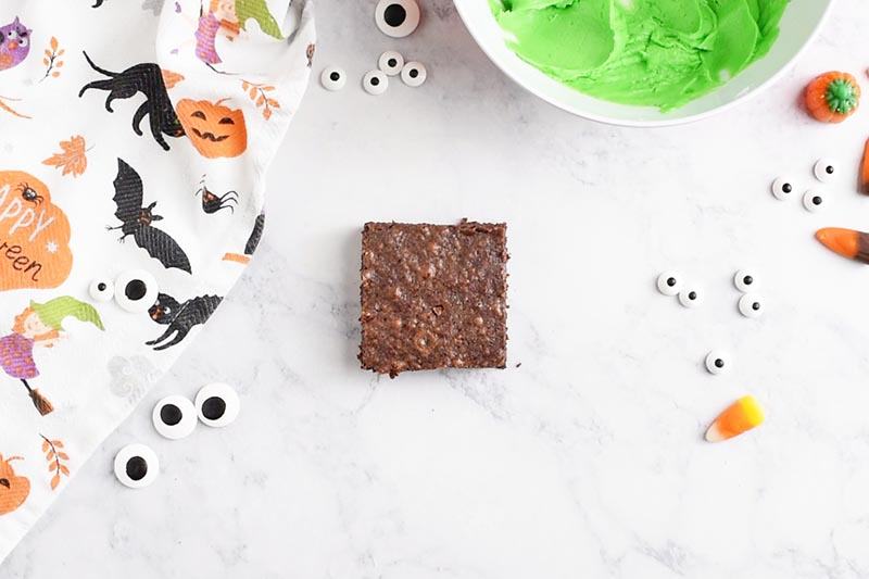 square brownie with candy eyeballs and Wilton leaf green icing on white marble countertop