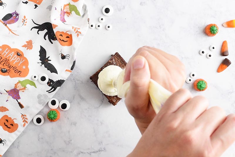 swirling whipped cream ghosts onto ghost halloween brownies with a pastry bag and Wilton Round Tip 2A, making easy halloween treats
